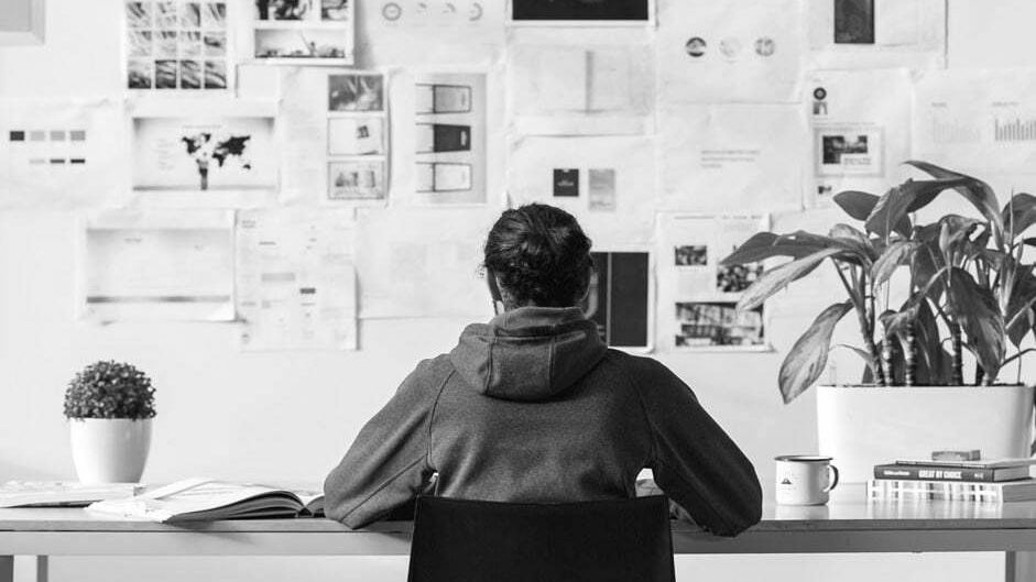 A designer working at a desk facing a wall pinned with layouts and mood-board references