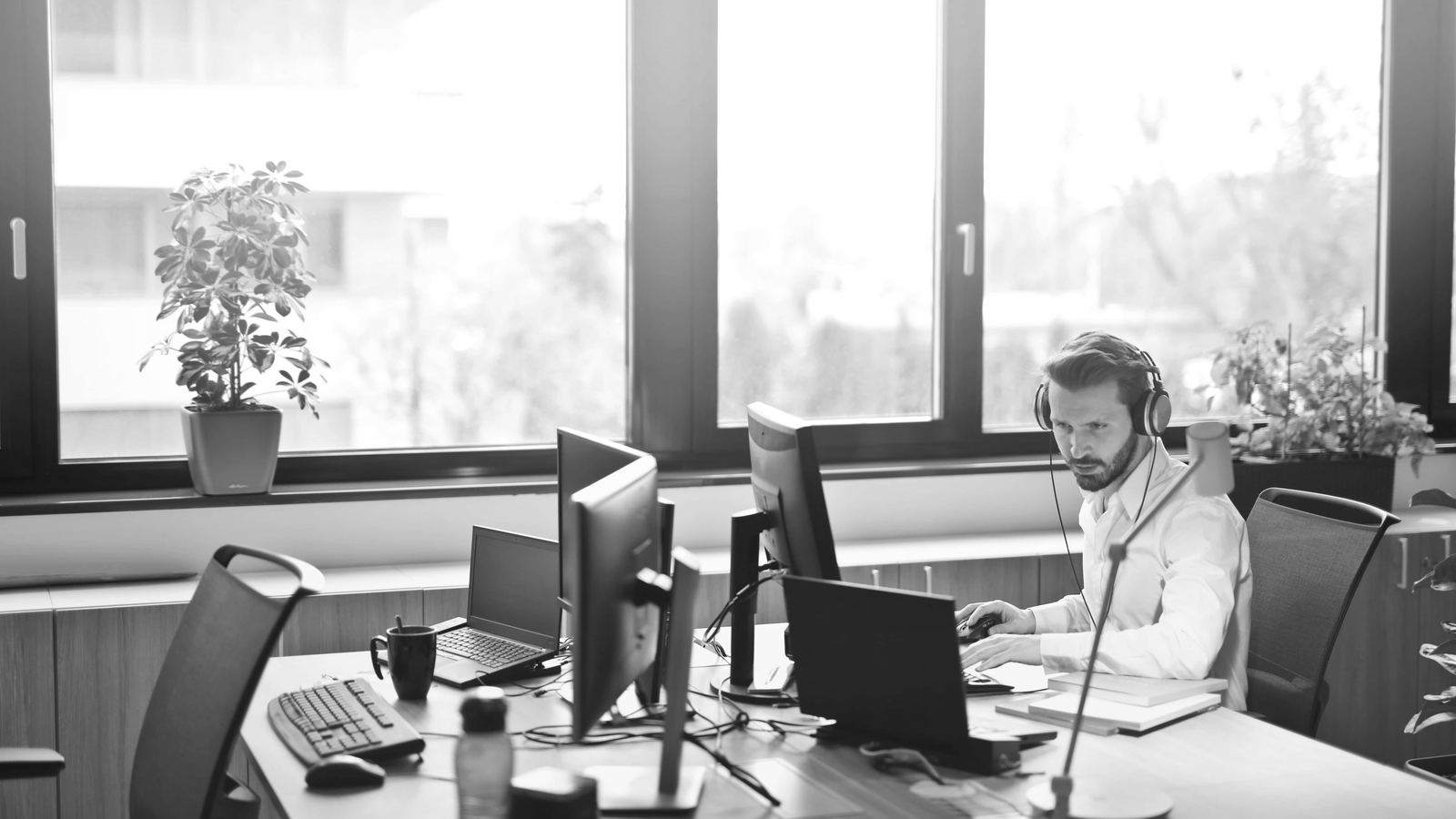 An analyst wearing a headset works across several monitors in a bright, open office