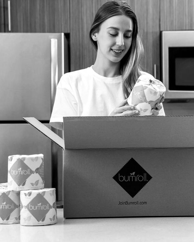 A customer unpacking a Bumroll subscription box of toilet paper in a kitchen