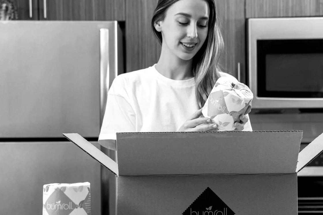 A customer unpacking a Bumroll subscription box of toilet paper in a kitchen